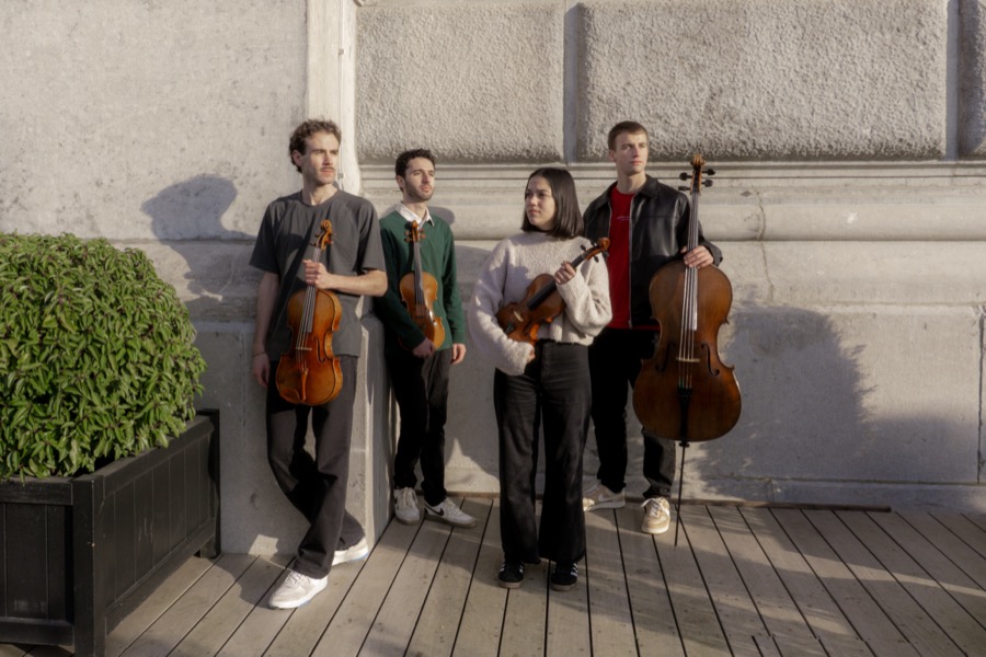 The quartet standing with their instruments against a stone wall on a wooden deck, in late afternoon sun