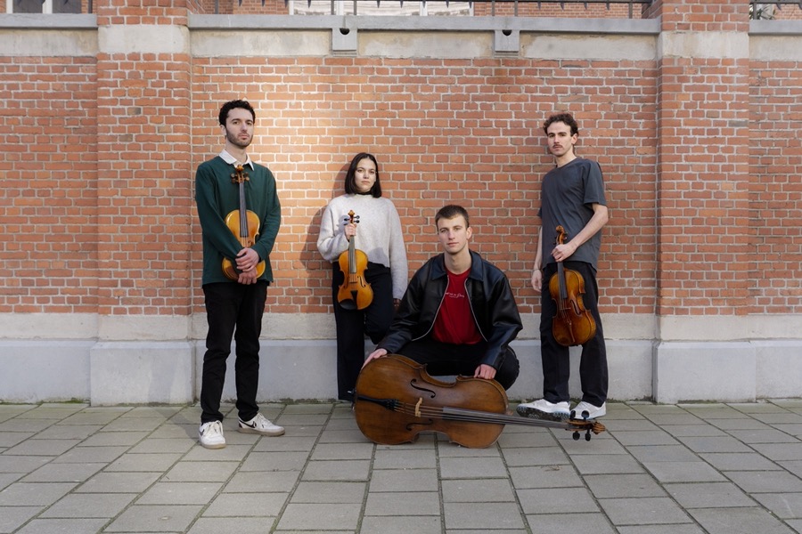 The quartet in front of a red brick wall, the cellist kneeling with the cello in front