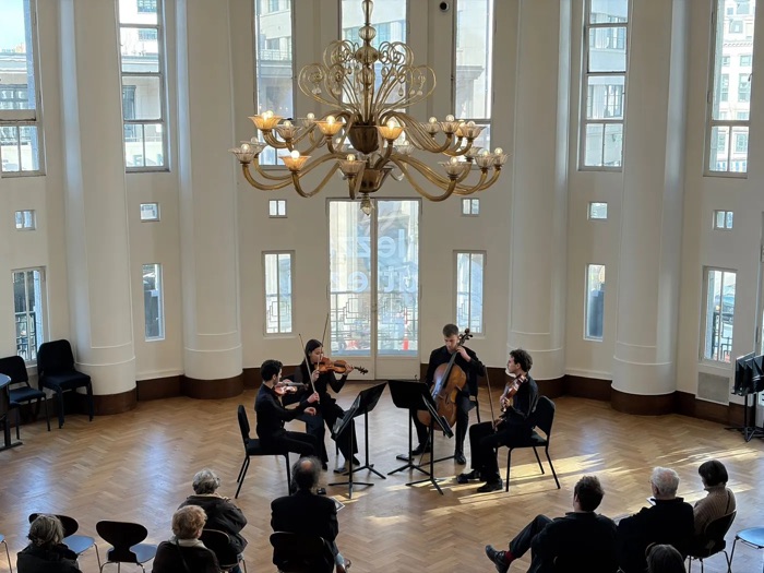 The quartet performing under a large chandelier in a bright round hall with tall windows, with the audience seated in front